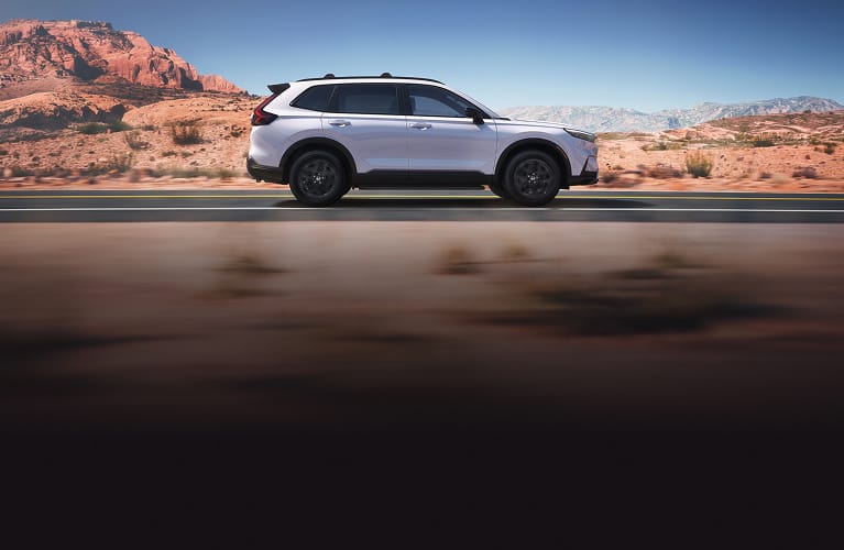 2026 Honda CR-V Sport Touring Hybrid in Platinum White Pearl profile driving on a scenic desert road (Compact Crossover SUV).